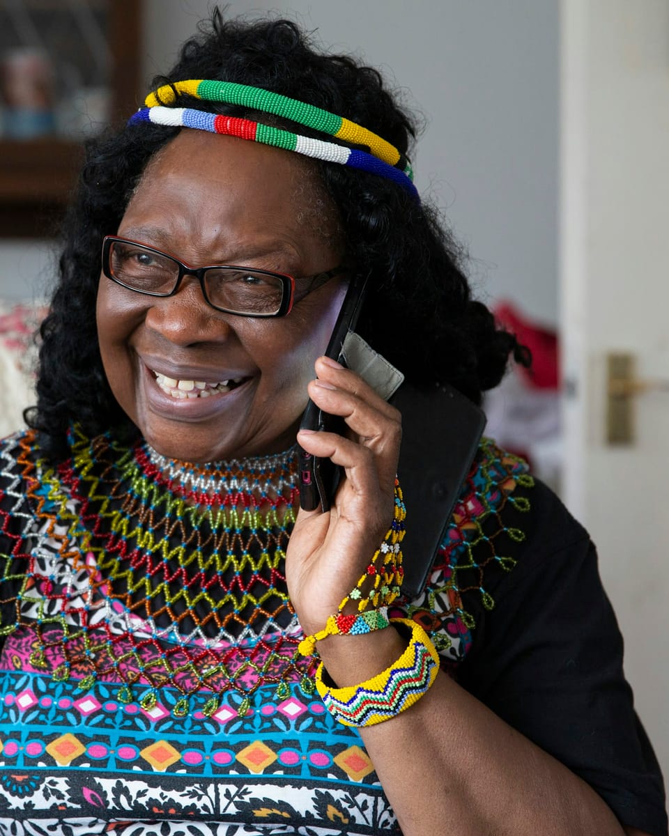 A woman wearing a beaded collar, laughing while on a phone call.