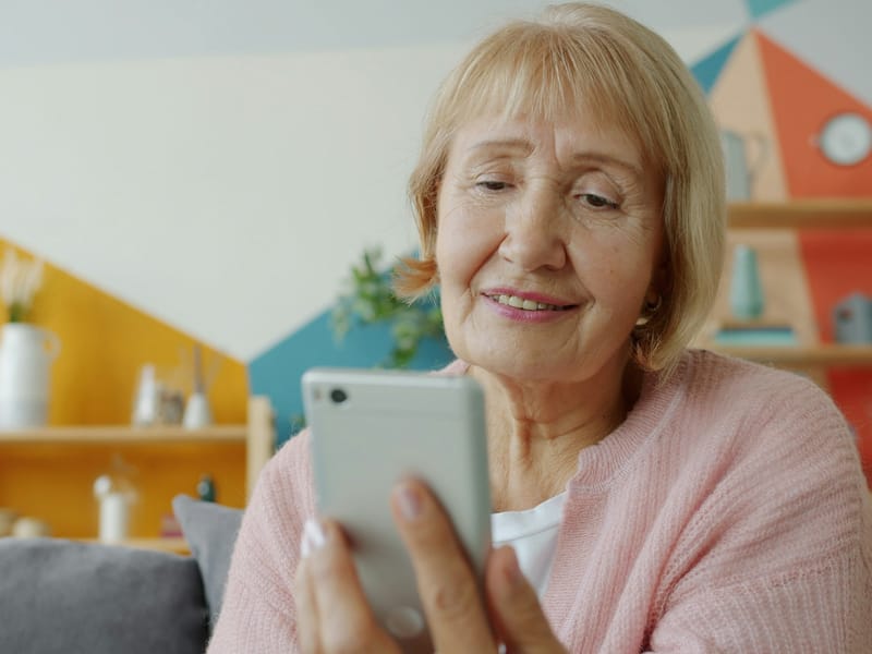 An older woman smiling as she reads something on her phone.