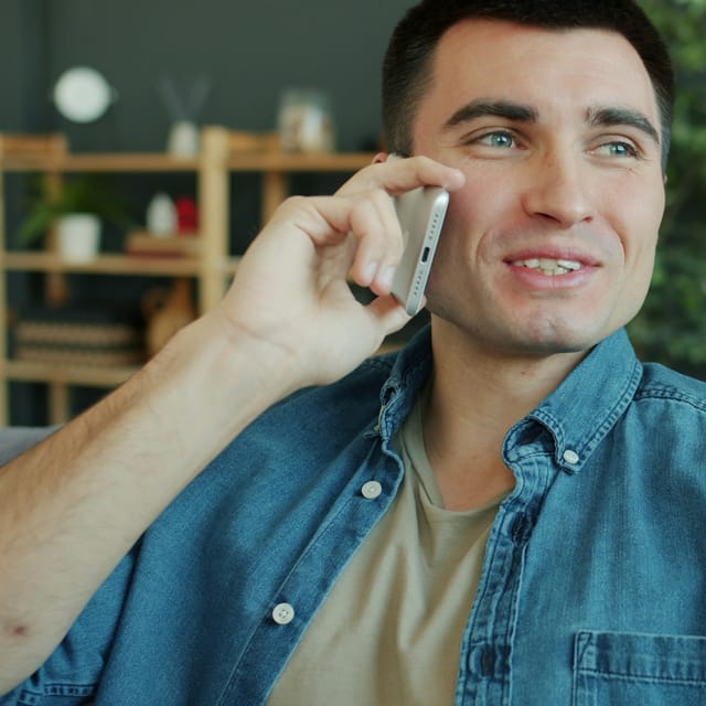 A man at home, smiling while he talks on his phone.