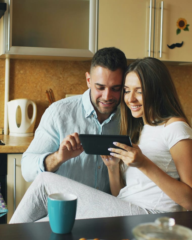 A couple at a kitchen counter, looking at a tablet together.